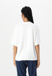 Losse witte T-shirt met korte mouwen en ronde hals, gemaakt van zachte stof. Zichtbare achternaaddetail, gecombineerd met marineblauwe broek.