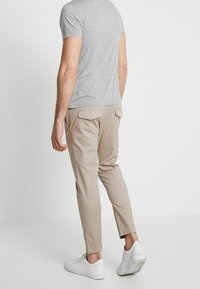 Beige chinos met een tapered fit, gemaakt van een katoenmix, gecombineerd met een lichtgrijs overhemd met korte mouwen en witte sneakers.