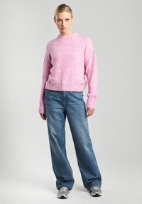 Pink knitted sweater with a crew neckline, ribbed cuffs, and relaxed fit, paired with loose blue denim jeans and grey sneakers.