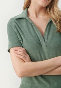 Grøn polo shirt i frotté stof med V-hals og korte ærmer. Har en blød tekstur og en afslappet pasform, velegnet til casual brug.