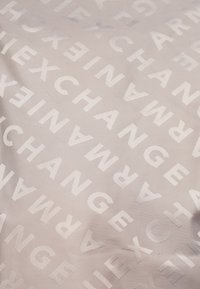 Textil cu un fundal gri deschis, cu litere ridicate și embosate care scriu "SCHIMBARE" și "EXCHANGE" în orientări variate.