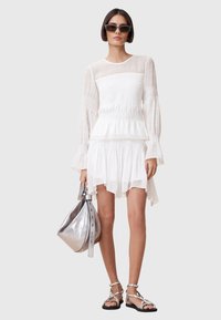 White, lightweight dress with a smocked bodice, long puffed sleeves, and layered hem. Paired with a metallic silver handbag and sandals.