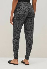 Zwarte legging met een gestructureerd zebra-printpatroon, met een slanke pasvorm en elastische tailleband, gecombineerd met platte zwarte sandalen.