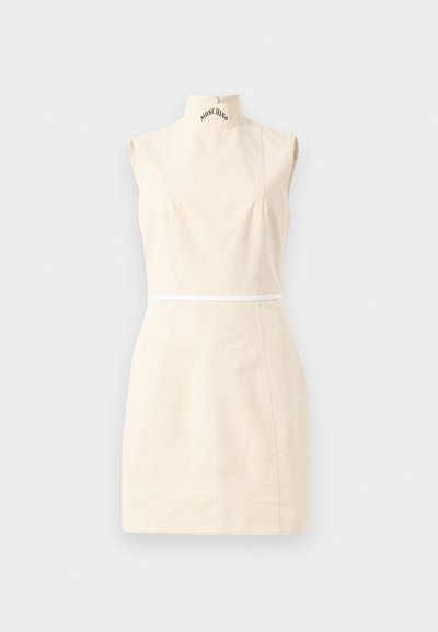 Αμάνικο μπεζ μίνι φόρεμα με ψηλό λαιμό, διακριτικές ραφές, λευκή λωρίδα στη μέση και κείμενο "MOSCHINO" στον γιακά.