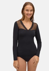 Top negro de manga larga con un yugo transparente de lunares, bordado de encaje en el escote y un diseño ajustado, combinado con pantalones negros.