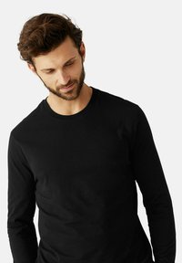 Zwart longsleeve t-shirt gemaakt van zacht katoen. Voorzien van een ronde halslijn en een slim fit ontwerp. Gladde textuur zonder patronen.