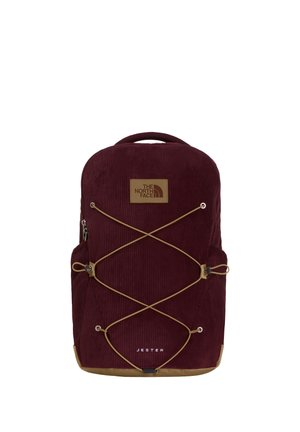 Sac à dos North Face Jester en velours côtelé rouge foncé avec fond beige, cordons élastiques à l'avant et poignée supérieure sur fond blanc.