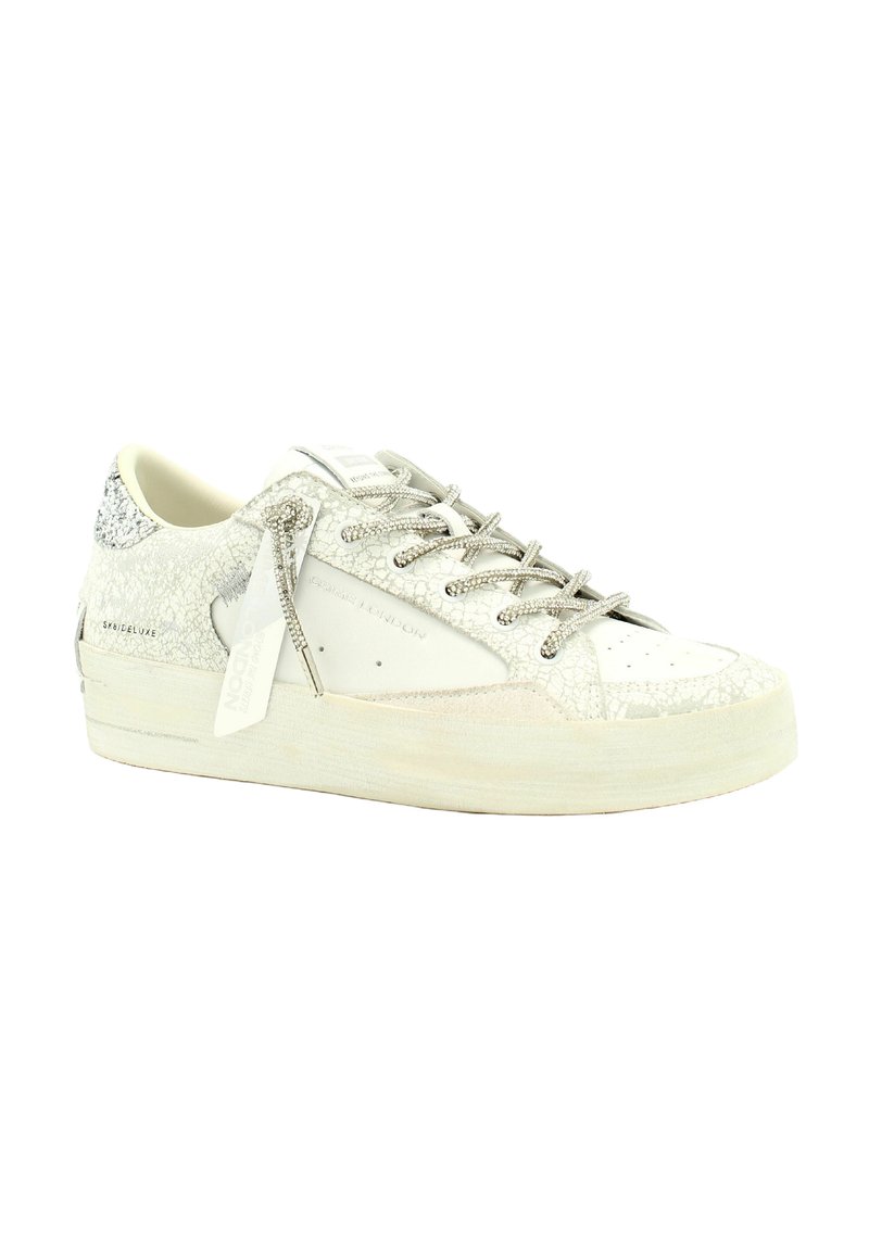 Zapatillas blancas con cordones, con una parte superior de cuero texturizado, acentos brillantes y una suela gruesa. Presenta cordones en tono plateado y una marca en el lateral.