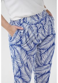 Blue and white patterned pants with palm leaf design, featuring an elastic waistband and side pockets. Smooth fabric texture.