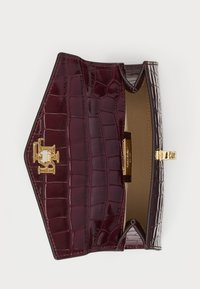 Burgundy bőrtáska fényes krokodilbélyegzett mintával, arany szemcsékkel és hajtogatható fedélzárással. A belső rész sima bélést tartalmaz.