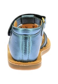 Sandalia azul metálica con textura suave, correas ajustables, parte trasera abierta y suela marrón. Presenta un diseño minimalista con forma redondeada.