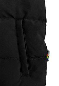 Zwarte geïsoleerde jas met een gladde textuur, met gestikte panelen en een zijzak. Er is een meerkleurig stoffen label aan bevestigd.