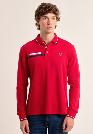 Polo rojo de manga larga con una botonera de tres botones, que presenta acentos en blanco y marino y un parche de logo en el pecho.