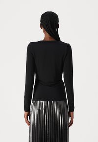 Maglietta nera a maniche lunghe con una texture liscia e una vestibilità rilassata, infilata in una gonna plissettata metallica, con dettagli sul retro.