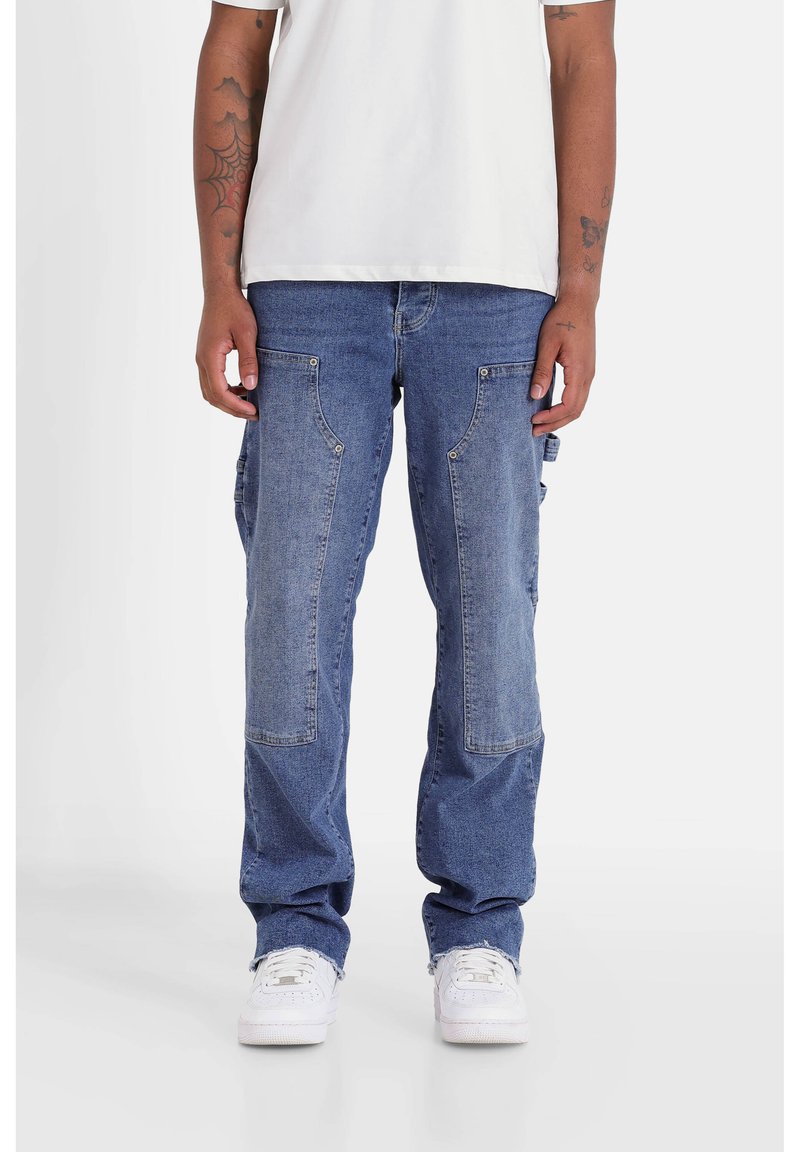 Pantalones cargo de denim azul con un corte holgado, bolsillos frontales y detalles de parches. Combinados con una camiseta blanca y zapatillas blancas.