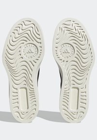 Paire de semelles de chaussures blanches avec rainures ondulées et texte circulaire du logo « Stella McCartney » entourant l'emblème Adidas sur chaque semelle.