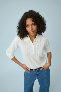 Pull-over blanc en tricot avec col et trois boutons, présentant un motif en chevrons texturé. Associé à un jean en denim bleu.