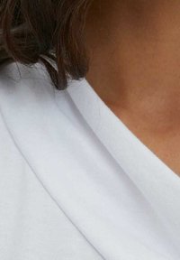 Tela blanca y suave dispuesta en un diseño de escote en v, mostrando una textura lisa y suaves pliegues alrededor del cuello, con un atisbo de piel debajo.