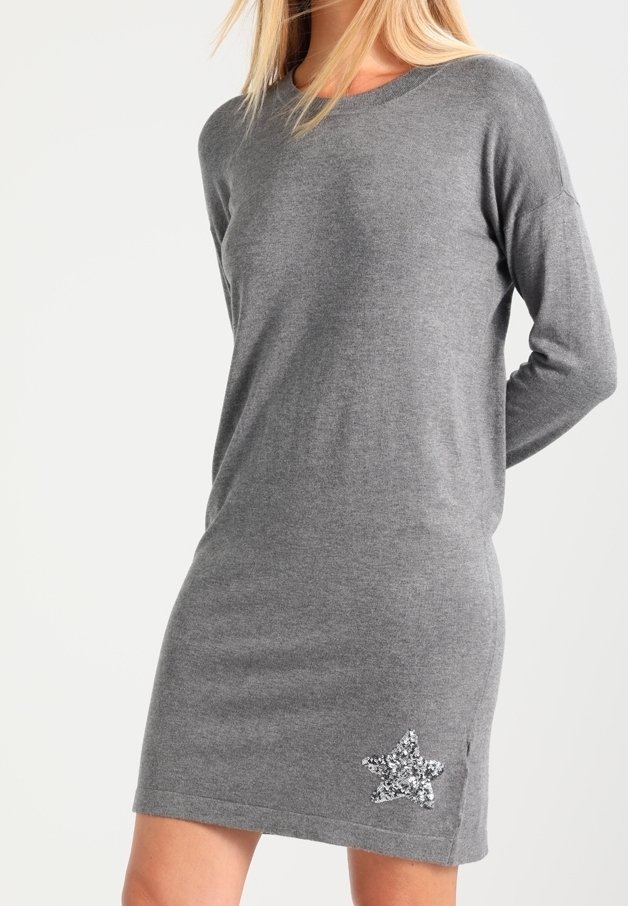 Femme portant une robe en maille grise à manches longues avec une étoile argentée en sequins près de l'ourlet sur le côté gauche.