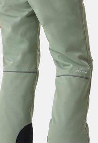 Grüne wasserdichte Hose mit glatter Textur, ausgestattet mit schwarzen Akzenten an der Unterschenkelpartie und einem reflektierenden STX™ 8000-Label an der Seitennaht.