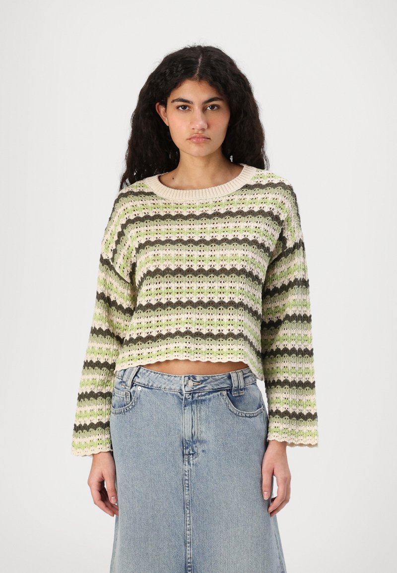 Heklet genser i grønn, krem og brun striper, med en bølget kant og lange ermer, paret med et lett blått denimskjørt.