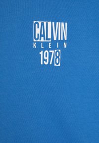 T-shirt in cotone blu con testo bianco: "CALVIN KLEIN 1978" in un carattere audace e moderno, con una superficie liscia e senza ulteriori motivi.