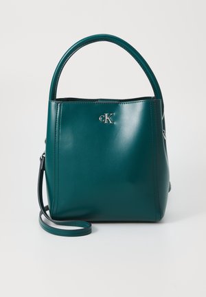 Turkusowa skórzana torba na ramię z zaokrąglonym uchwytem, odpinanym paskiem na ramię oraz srebrnym logo CK na przodzie.