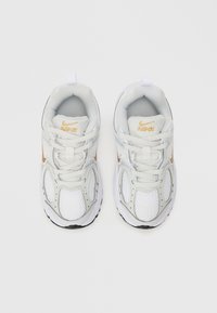 Zapatillas deportivas blancas con parte superior de malla, acentos plateados y suela negra. Cuentan con cordones y un collar acolchado para mayor soporte. Logo de Nike presente.