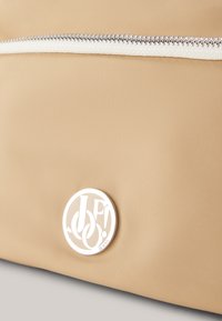 Borsa in tessuto beige con superficie testurizzata, una cerniera bianca e un logo circolare bianco con la scritta "JP!" e "JEANS".