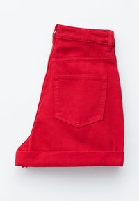 Jean en denim rouge plié montrant une poche arrière et des passants de ceinture sur fond blanc.