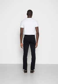 T-shirt bianco a maniche corte abbinato a pantaloni blu scuro. I pantaloni presentano tasche posteriori e un design slim fit. Scarpe nere completano l'outfit.