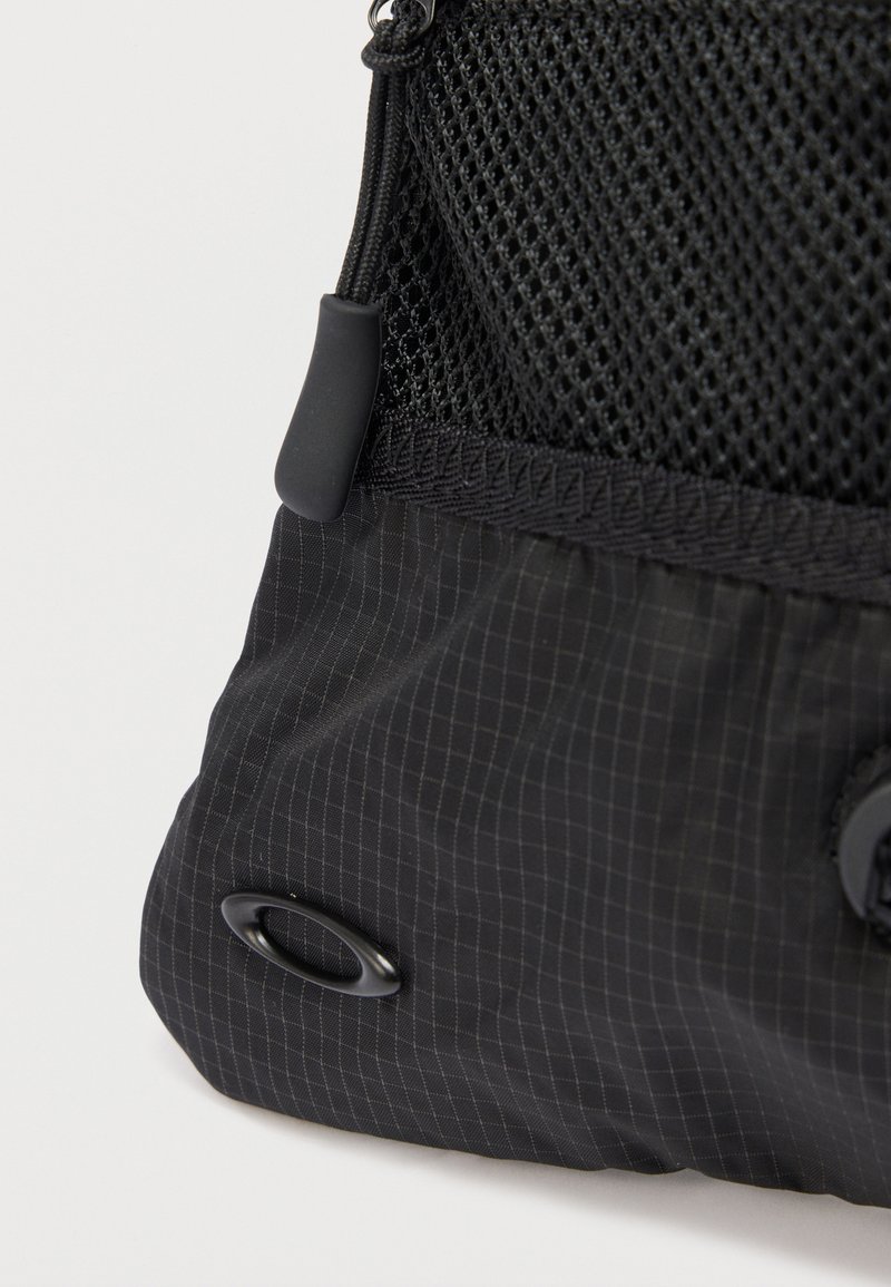 Angolo di borsa in tessuto nero con sezione superiore in rete, cordino della cerniera con impugnatura in gomma e piccolo logo ovale nero su tessuto inferiore testurizzato.