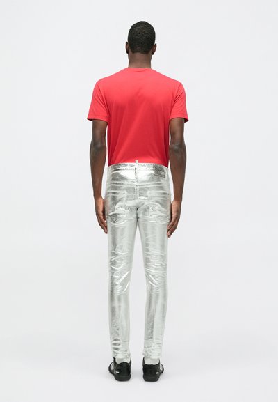 Punane lühikeste varrukatega T-särk ja läikivad hõbedased kitsad teksad, millel on sile tekstuur metallilise viimistlusega ja kaks tagakotti.