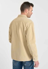 Beige corduroy shirt met lange mouwen, een puntige kraag en knoopaccenten, gezien vanuit de achterkant. Textuur, relaxed fit.