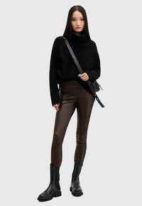 Kobieta ubrana w czarny sweter z golfem, brązowe skórzane legginsy, czarne botki oraz torebkę na ramię z szerokim paskiem.