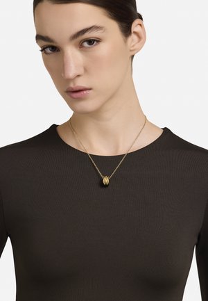 Kuldne kaelakee tekstuurse ripatsiga, kantud musta kitsast topi kohal. Disainis on õrn kett ja silmatorkav keskne detail.