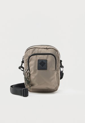 Lille beige Columbia crossbody taske med sort kant, front lynlåslomme, flettede lynlåstrække og justerbar sort rem på hvid baggrund.