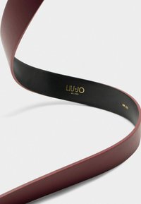 Cintura in pelle borgogna con texture liscia, dotata di un interno nero. Il logo dorato "LIU JO MILANO" e l'etichetta "TAGLIA UNICA" sono visibili.