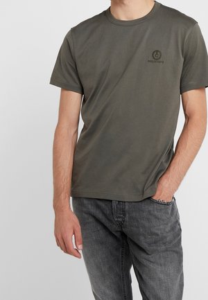 Olivengrøn kortærmet t-shirt med rund hals og logo på venstre bryst; parret med mørk denim jeans.