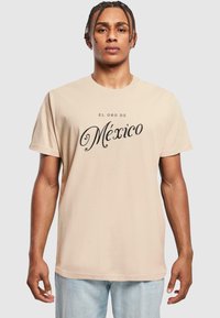 Beige színű, rövid ujjú pamut póló, melynek elején fekete, díszes betűtípussal "El Oro de México" felirat található.
