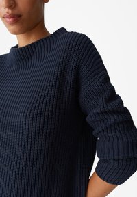 Maglione lavorato a maglia blu navy con texture a costine, design con scollo a barca e maniche di larghezza media, caratterizzato da una vestibilità rilassata e cuciture dettagliate.