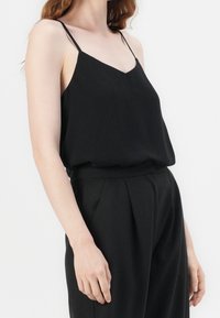 Top nero senza maniche con scollatura a V, dotato di spalline sottili e vestibilità rilassata, realizzato in tessuto morbido. Design minimalista senza fantasie.