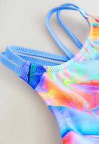 Flerfärgad badklädsel med abstrakta tie-dye-mönster i nyanser av blått, rosa, orange och grönt. Har tunna, kontrasterande blå remmar.