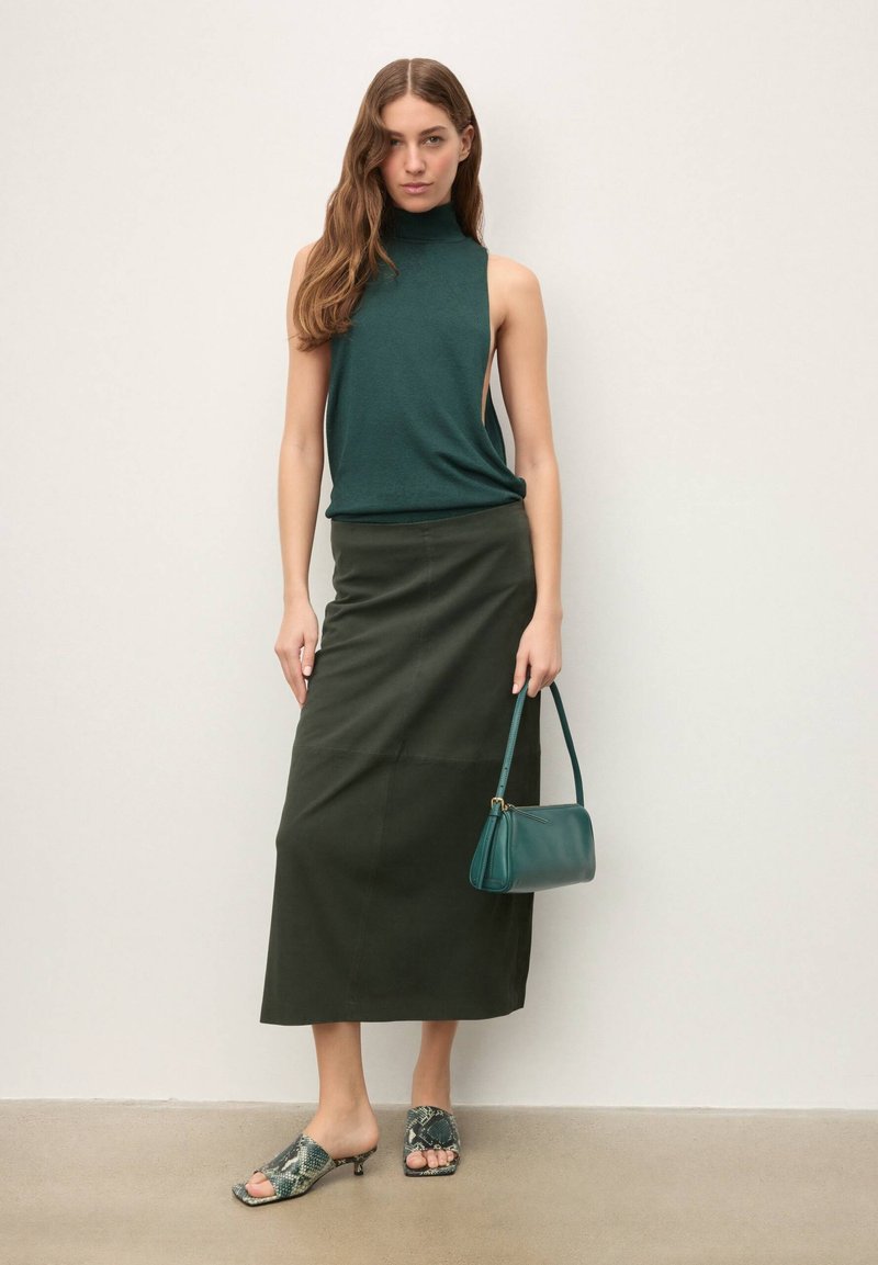 Haut sans manches vert foncé avec col montant, jupe midi vert olive, sac à main bleu sarcelle et sandales à talons avec motif. Textures de tissus lisses.