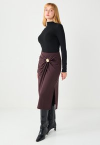 Black long-sleeve top paired with a burgundy midi skirt featuring a knot detail and a side slit, complemented by knee-high black boots.