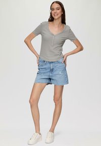 Grijze geribbelde T-shirt met een ronde halslijn en knoopaccenten, gecombineerd met lichtblauwe denim shorts met rafelige zomen en versleten details.