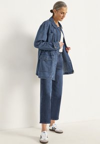 Denim jacket with a collared neckline, two front pockets, and button closures, paired with matching denim pants and white sneakers.