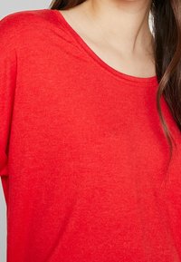 Red short-sleeve shirt with a round neckline, made of soft, textured fabric. Features a relaxed fit and smooth finish.