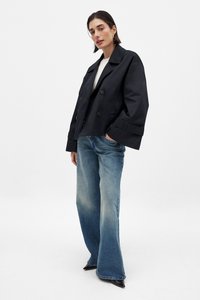 Svart dubbelknäppt kort trenchcoat med vida ärmar, i kombination med ljusblå utsvängda jeans. Slät textur, minimalistisk design.