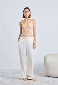 Body in pizzo beige chiaro con spalline sottili, abbinato a pantaloni ampi color crema con rifiniture nere. Tessuto dalla texture morbida.